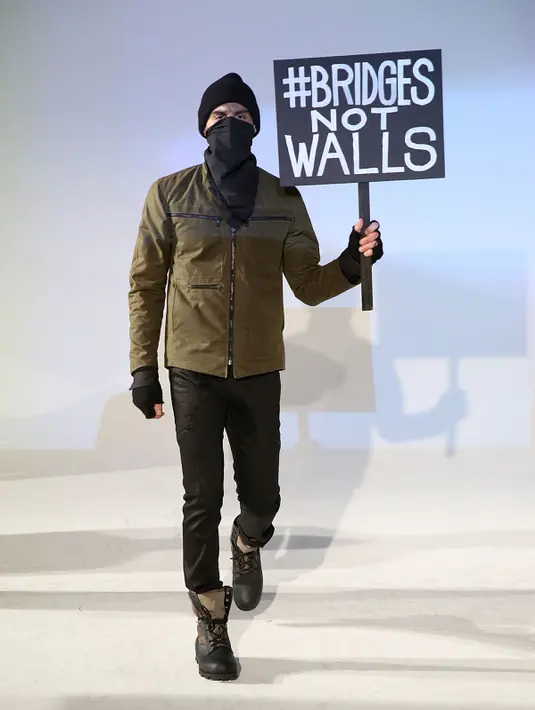 Seorang model berpose dengan poster #Bridges Not Wals saat presentasi desainer Robert James dalam NYFW di New York, (30/1). Poster ini menyindir program Donald Trump yang akan membangun tembok perbatasan dengan Meksiko. (Robin Marchant Getty Images/AFP)