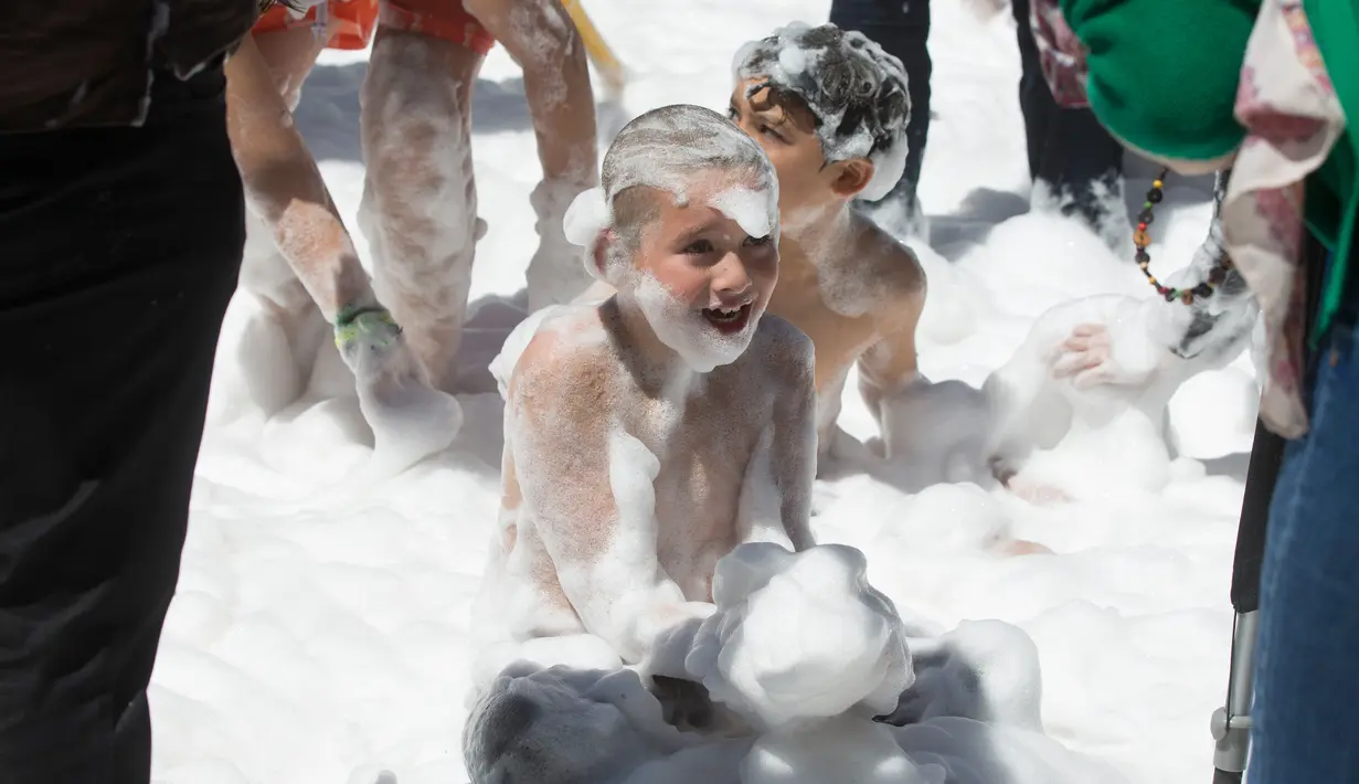 Seorang anak bermain busa yang disemprotkan oleh petugas pemadam kebakaran selama pesta di distrik Malasana Madrid, Spanyol, (4/5/2019). (AP Photo/Paul White)