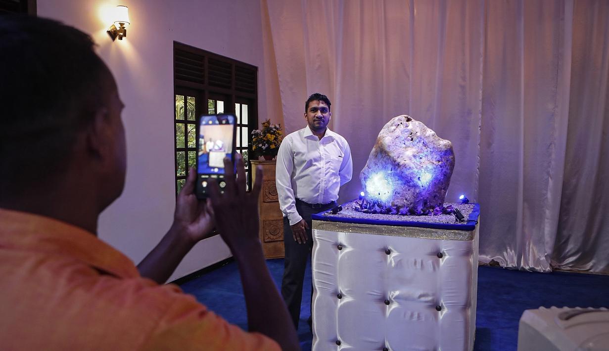 Penggemar permata Sri Lanka mengambil foto berdiri di samping safir biru korundum alami seberat 310 kilogram di Horana, sekitar 41 km dari selatan Kolombo, pada 12 Desember 2021. Batu safir itu ditemukan di daerah Ratnapura yang kaya permata. (AP Photo/Eranga Jayawardena)
