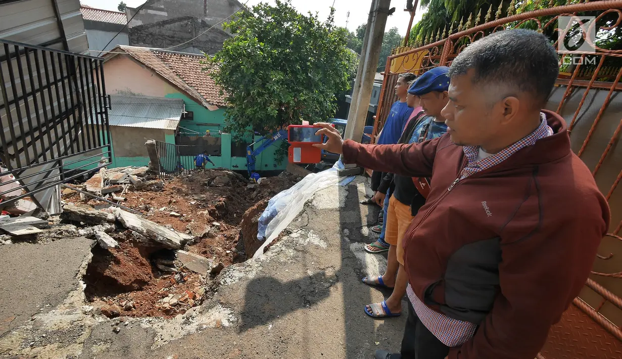 Seorang warga mengambil gambar kondisi tanah longsor di Perumahan Pesona Kalisari, Pasar Rebo, Jakarta, Selasa (27/11). Intensitas hujan yang tinggi mengakibatkan sebidang tanah di wilayah tersebut longsor. (Liputan6.com/Herman Zakharia)
