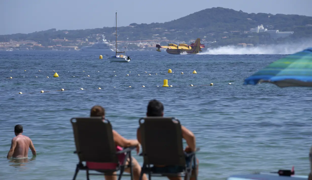 Wisatawan menyaksikan pesawat pelempar air mengisi tangkinya di pantai di Sainte-Maxime, Prancis selatan, Rabu (18/8/2021). Lebih dari 1.100 petugas pemadam kebakaran berjuang melawan api dan ribuan turis dan penduduk lokal dievakuasi ke daerah yang lebih aman. (AP Photo/Daniel Cole)