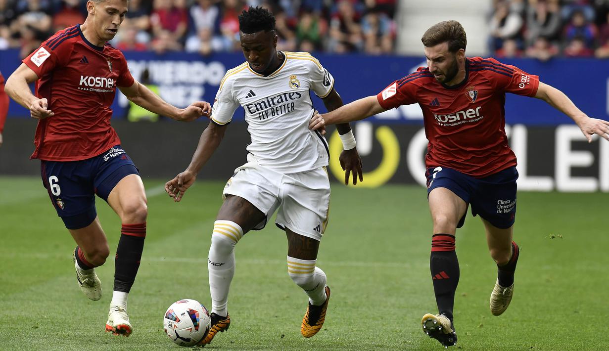 Pemain Real Madrid, Vinicius Junior, berebut bola dengan pemain Osasuna, Lucas Torro dan Jon Moncayola, pada laga pekan ke-29 La Liga 2023/2024 di Stadion El Sadar, Sabtu (16/03/2024). Vinicius Junior tampil gemilang dengan memborong dua gol. (AP Photo/Alvaro Barrientos)