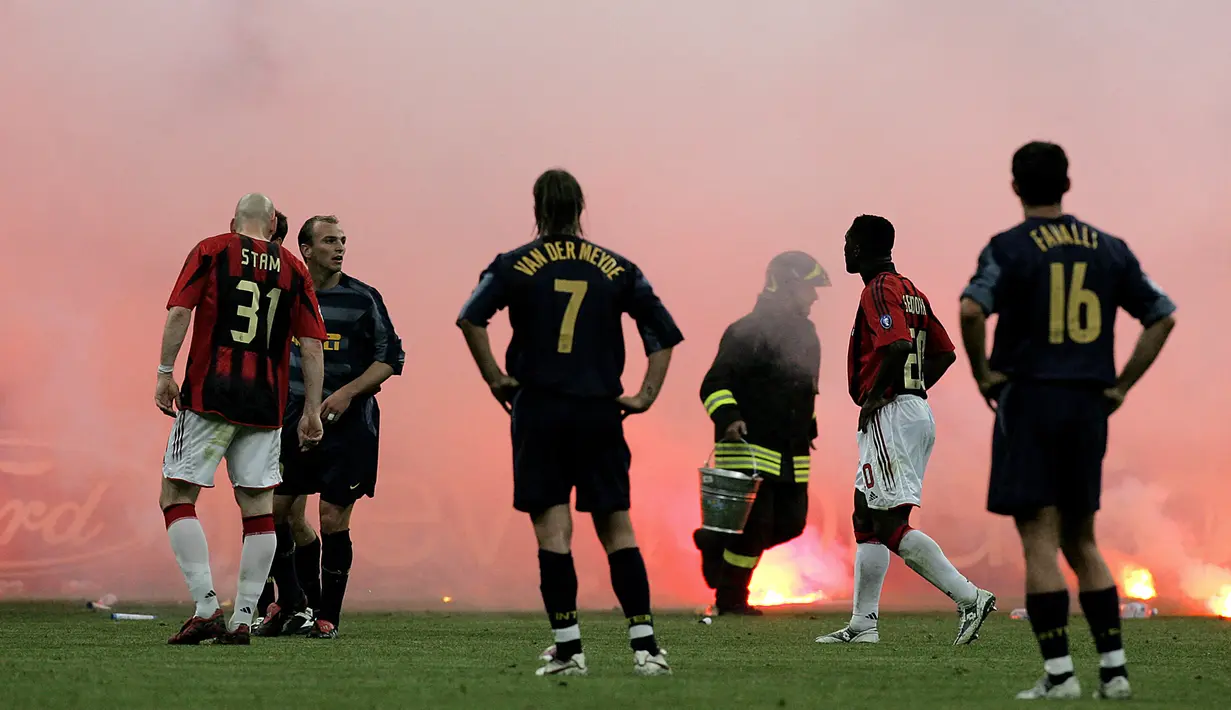 Seorang petugas berusaha mematikan dan mengumpulkan flare yang dilontarkan fans fanatik Inter Milan saat menghadapi AC Milan pada laga leg kedua babak perempatfinal Liga Champions 2004/2005 di San Siro Stadium, Milan (12/4/2005). AC Milan masih unggul 1-0 berkat gol Andriy Shevchenko saat laga dihentikan akibat ulah fans fanatik Inter Milan yang melempar flare ke dalam lapangan. (AFP/Filippo Monteforte)