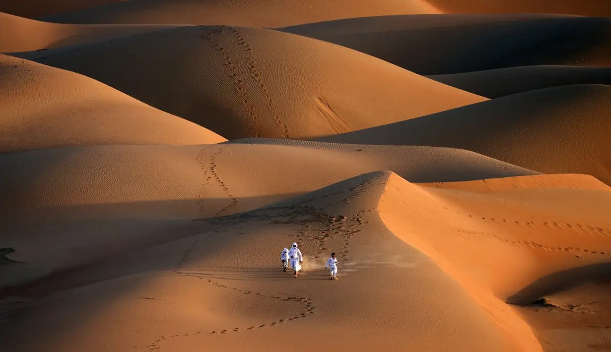 Sejumlah pemuda berlari melintasi gundukan pasir di Gurun Liwa, Abu Dhabi, Uni Emirat Arab, Sabtu (9/1/2021). Elang telah terhubung dengan budaya Uni Emirat Arab selama berabad-abad. (Karim SAHIB/AFP)