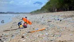 Sejumlah pengunjung berada di antara sampah kiriman yang terdampar memenuhi pesisir pantai Kuta, Bali, Kamis (31/12/2020). Menjelang pergantian tahun baru, Pantai Kuta hanya terlihat beberapa wisatawan, namun tumpukan sampah kiriman tersebar di sepanjang bibir pantai. (SONNY TUMBELAKA / AFP)