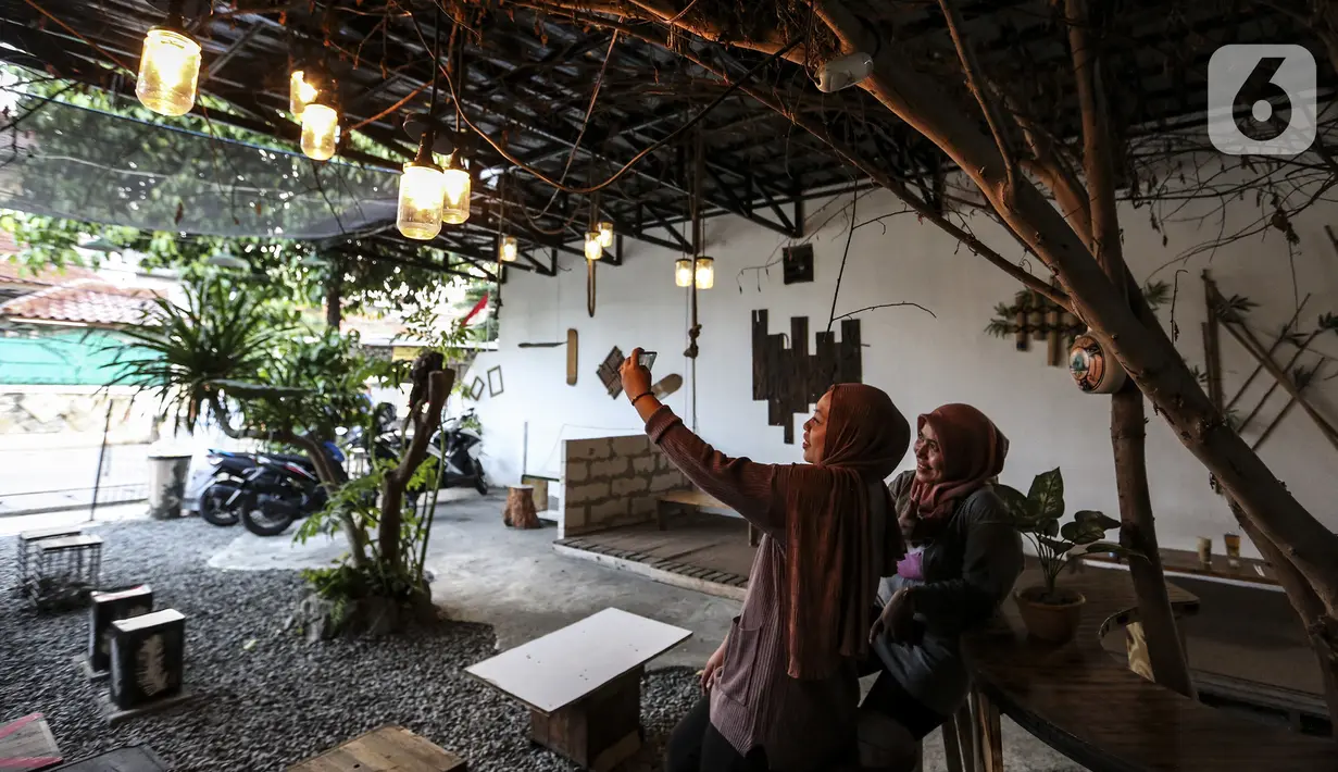 Pengunjung berswafoto di Kedai Poci (KEPO), Hj Kelik, Kelapa Dua Srengseng, Jakarta Barat, Sabtu (18/9/2021). Pemilik usaha kafe ini keluhkan sepi dikarenakan baru bisa membuka usahanya belum lama ini. (Liputan6.com/Johan Tallo)