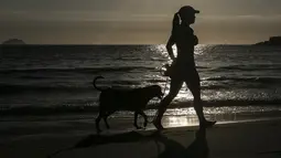 Seorang wanita berjalan dengan anjingnya di sepanjang Copacabana selama gelombang panas di Rio de Janeiro, Brasil, pada hari libur kota Saint Sebastian, Kamis pagi (20/1/2022). (AP Photo/Bruna Prado)