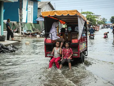 Anak-anak duduk di belakang kendaraan yang melintas saat banjir rob di Muara Angke, Jakarta, Jumat (25/11/2022). Badan Penanggulangan Bencana Daerah (BPBD) DKI Jakarta mengimbau agar warga di pesisir Jakarta mengantisipasi banjir pesisir atau rob selama 22-28 November 2022. (Liputan6.com/Faizal Fanani)