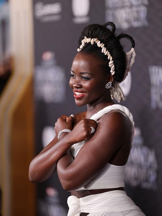 Lupita Nyong'o berpose saat menghadiri pemutaran perdana film Black Panther: Wakanda Forever" di Dolby Theatre di Los Angeles pada Rabu, 26 Oktober 2022. Rambut brunette-nya ditata dengan twist updo yang beraksen dengan ikat kepala yang terbuat dari kerang. (Jesse Grant/Getty Images for Disney/AFP)