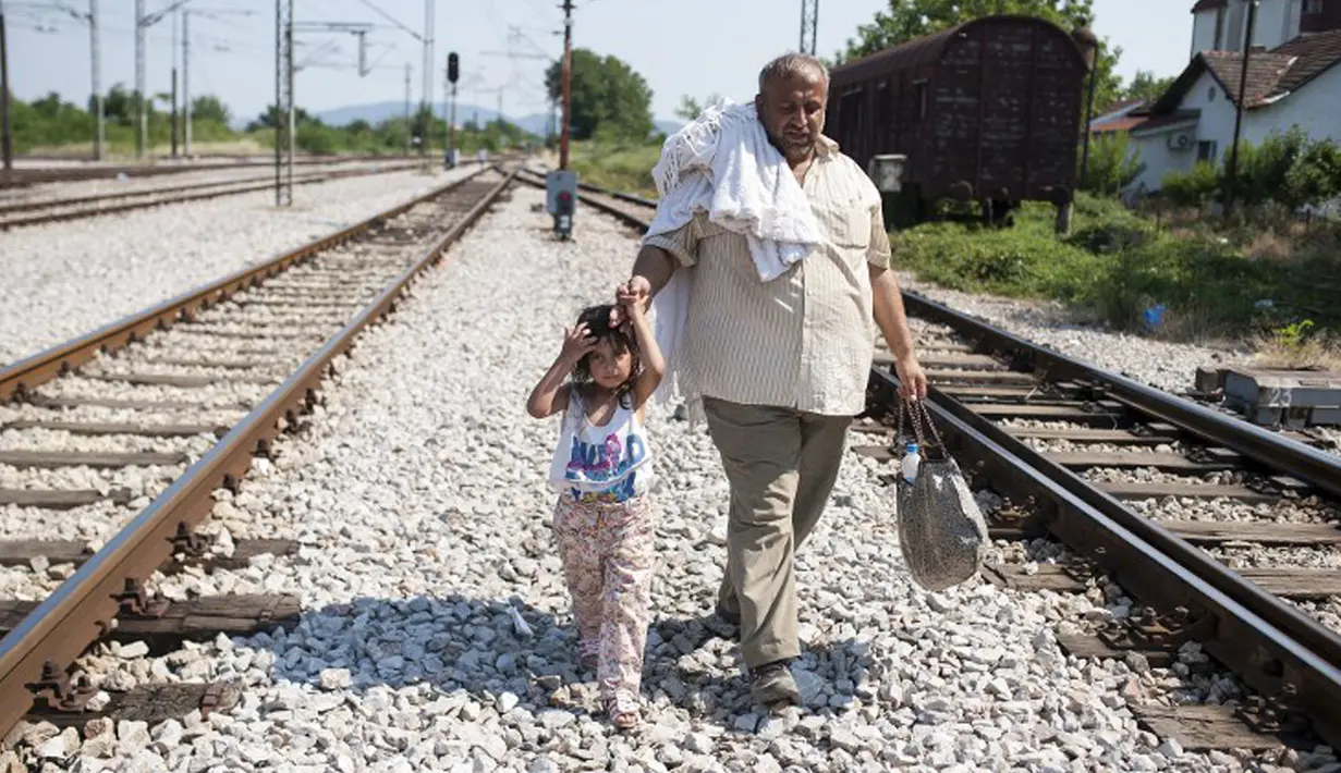 Seorang imigran bersama anaknya berjalan menyusuri rel kereta api saat perjalanan menuju Gevgelija, wilayah perbatasan Macedonia-Yunani, Kamis (9/7). Mereka menempuh ribuan kilometer agar dapat mengejar kereta tujuan Serbia (AFP PHOTO/Robert ATANASOVSKI)