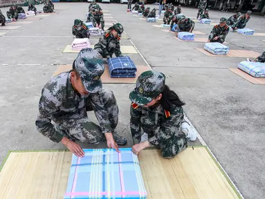 Tentara (kiri) mengajari mahasiswa baru melipat selimut selama sesi pelatihan militer di sebuah kampus di Yangzhou, Jiangsu, China, Jumat (6/9/2019). China memilih pelatihan militer atau dikenal dengan istilah 'Junxun' sebagai program orientasi mahasiswa baru. (STR/AFP)