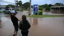 Orang-orang berdiri di tepi air banjir di sepanjang Jalan Haleiwa di Hawaii (9/3/2021). Hujan deras telah menggenangi beberapa bagian Hawaii selama beberapa hari terakhir. (Jamm Aquino/Honolulu Star-Advertiser via AP)