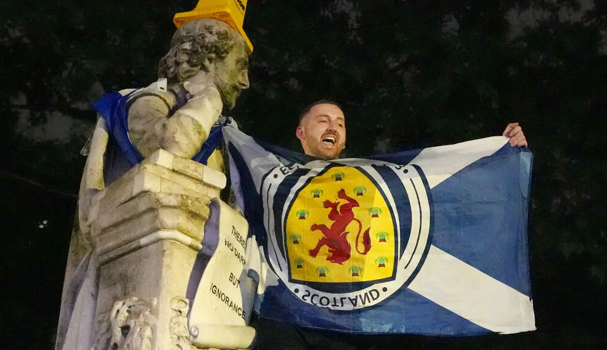 Seorang pendukung Skotlandia mengibarkan bendera di patung William Shakespeare di Leicester Square, London, Jumat (18/6/2021). (AP/Kirsty Wigglesworth)