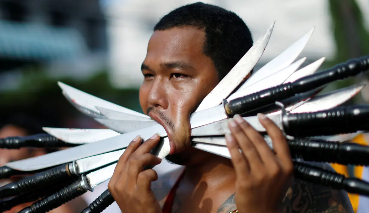 Seorang pemuja dari Kuil Samkong menusukkan senjata tajam pada pipinya ketika beratraksi dalam Festival Vegetarian di Phuket, Thailand, Selasa (4/10). (REUTERS/Jorge Silva)
