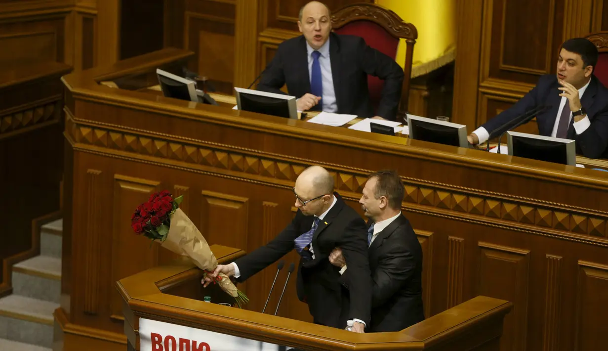Seorang anggota parlemen, Oleg Barna mencoba menarik dan menggendong PM Arseny Yatsenyuk di podium Majelis Tinggi Parlemen Ukraina, 11 Desember 2015. Sebelum diseret, PM Yatsenyuk diberi karangan bunga oleh anggota parlemen itu (REUTERS/Valentyn Ogirenko)
