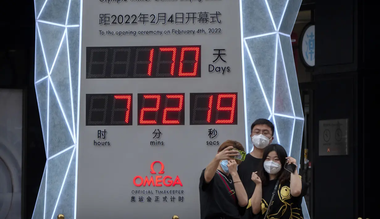 Orang-orang yang memakai masker untuk melindungi diri dari COVID-19 berpose di depan layar yang menunjukkan jam hitung mundur ke Olimpiade Musim Dingin 2022 di Beijing (18/8/2021).  Pejabat tinggi Beijing menegaskan kembali perlunya anti-pencegahan yang ketat. (AP Photo/Mark Schiefelbein)
