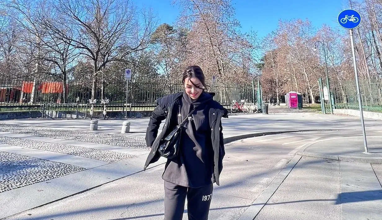 Gaya serba hitam Ayu Ting Ting saat berlibur. Ia mengenakan hoodie, yang ditumpuknya lagi dengan jaket, dipadu mengenakan sweat pants, sling bag hitam, dan sneakers putih. [Foto: Instagram/ayutingting92]