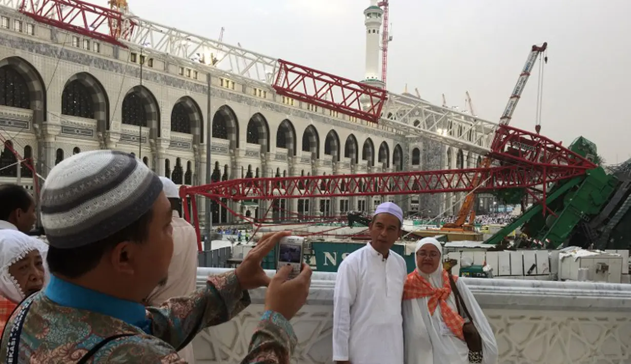 Calon jemaah haji foto bersama dengan latar berlakang crane yang roboh di Masjidil  Haram, Kota Mekah,  Arab Saudi (9/12/2015). Sebanyak 107 calon jemaah haji meninggal dunia akibat crane jatuh karena cuaca buruk. (AFP PHOTO / STR)