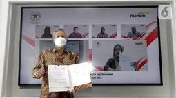 Rohan Hafas menunjukkan MoU Kerjasama Kemensetneg dan Bank Mandiri disaksikan Mensesneg Pratikno, Sekretaris Setya Utama, Deputi Administrasi Aparatur Kemensetneg Nanik Purwanti, Dirut Bank Mandiri Darmawan Junaidi dan Wadirut (di layar LED) di Jakarta, Kamis (15/7/2021). (Liputan6.com/HO/Mandiri)