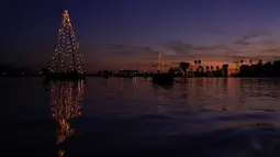 Sebuah pohon Natal mengambang yang terbuat dari lampu memantul di air di Long Beach, California, Minggu (19/12/2021). Sambut Natal, pantai di California menghiasi pantainya dengan hiasan lampu pohon Natal. (AP Photo/Ashley Landis)