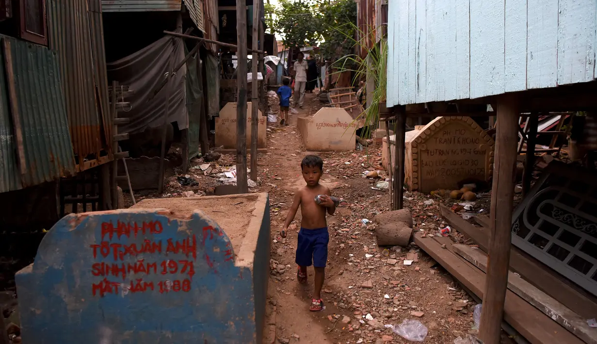 Seorang anak melewati bangunan rumah di sebuah kuburan di Phnom Penh, Kamboja pada 21 Mei 2019. Pemakaman menjadi tempat peristirahatan abadi bagi orang mati, tetapi area pemakaman ini menjelma sebagai tempat tinggal untuk bertahan hidup bagi mereka yang didera kemiskinan. (TANG CHHIN Sothy/AFP)