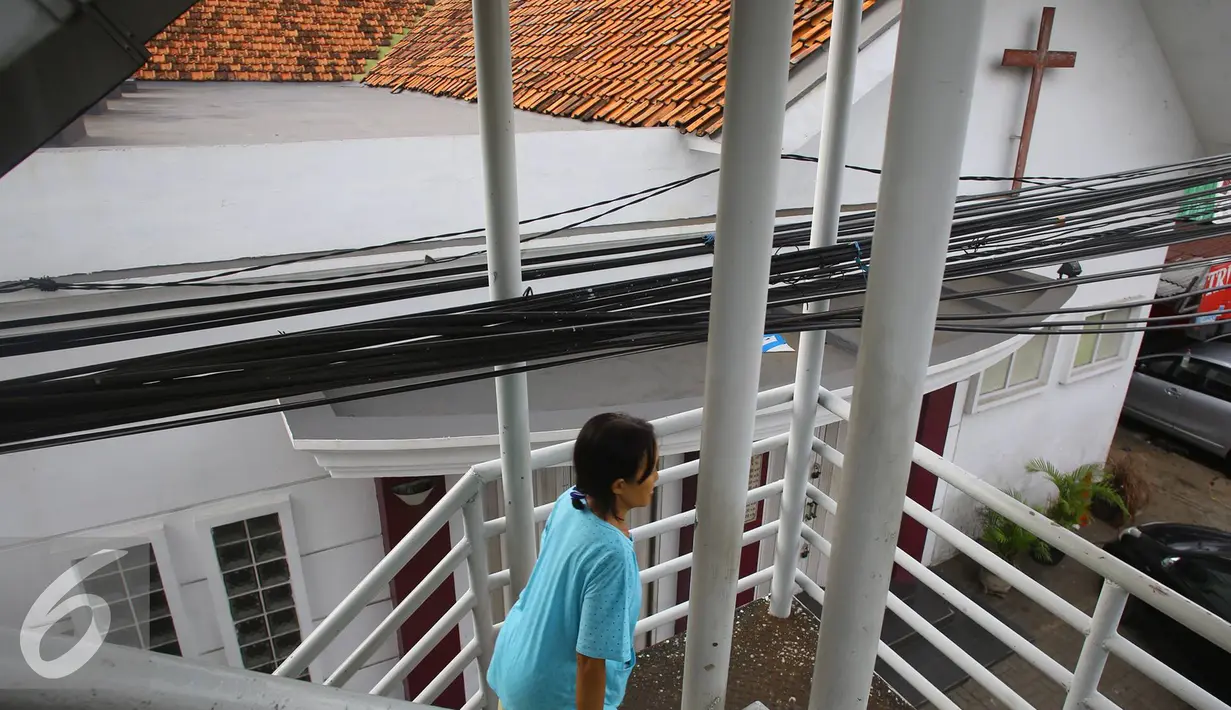 Warga melintas di bawah instalasi kabel yang menjuntai di JPO kawasan Cawang, Jakarta, Rabu (25/1). Selain mengganggu kenyamanan, buruknya penempatan instalasi kabel tersebut juga berbahaya bagi keselamatan pengguna JPO. (Liputan6.com/Immanuel Antonius)