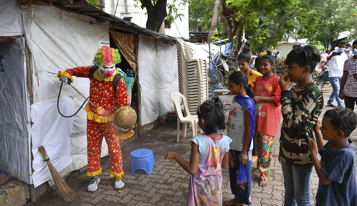 Relawan pekerja sosial, Ashok Kurmi berinteraksi dengan anak-anak saat mendisinfeksi ruang publik di daerah kumuh Mumbai pada 2 Juni 2021. Kurmi turun tangan memerangi virus Corona COVID-19 di daerah kumuh Mumbai menggunakan aksesori yang tidak biasa, yaitu kostum badut. (INDRANIL MUKHERJEE/AFP)