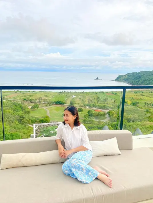 Prilly Latuconsina menikmati waktunya melihat keindahan alam. Ia mengenakan atasan kemeja lengan panjang berwarna putih dengan celana panjang bermotif batik bernuansa biru. Foto: Instagram.