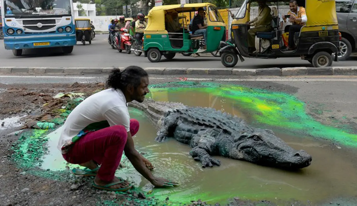 Seniman Baadal Nanjundaswamy menyelesaikan boneka buaya di atas jalan berlubang di Sultanpalya, Bangalore, India, Kamis (18/6/2015). Pria tersebut mendesak pemerintah agar segera memperbaiki jalan yang rusak. (AFP PHOTO/ Manjunath KIRAN)