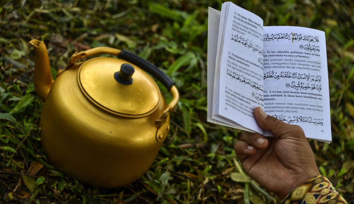 Seorang pria membaca Alquran pada peringatan 16 tahun gempa bumi dan tsunami Aceh di sebuah kuburan massal di Siron, Sabtu (26/12/2020).  Peringatan di tengah pandemi COVID-19 itu tetap berlangsung secara sederhana melalui kegiatan ziarah kubur. (CHAIDEER MAHYUDDIN/AFP)