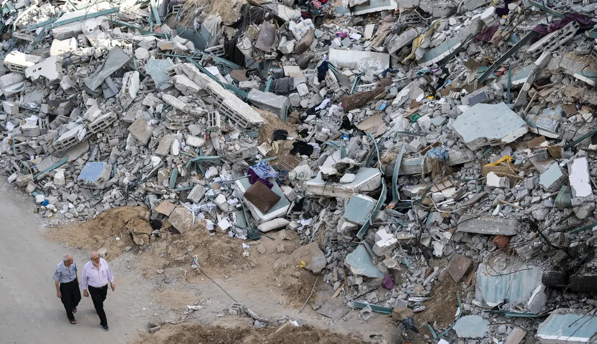 Orang-orang berjalan di dekat puing-puing gedung al-Jalaa menyusul gencatan senjata yang dicapai setelah perang 11 hari antara Hamas dan Israel, di Kota Gaza, Jumat (21/5/2021). Bangunan itu menampung biro Associated Press di Kota Gaza selama 15 tahun. (AP Photo/John Minchillo)