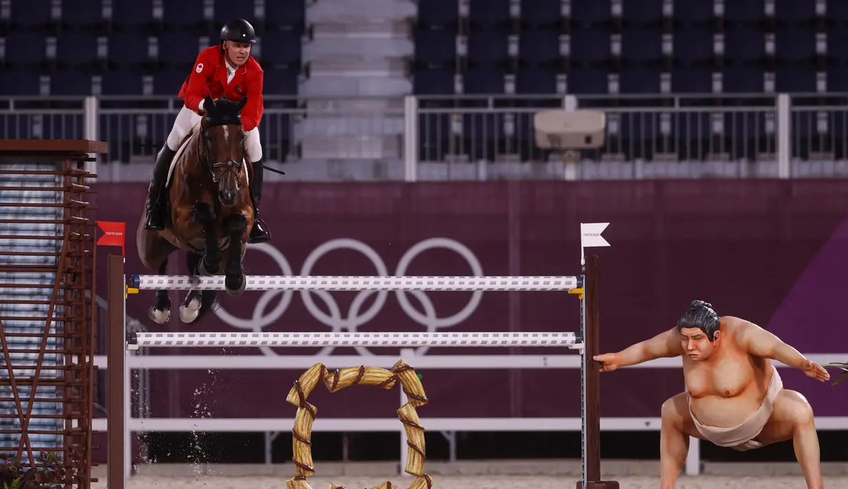 Atlet berkuda Kanada Mario Deslauriers mengendarai Bardolina 2 melewati patung pesumo dalam kualifikasi individu lompat berkuda Olimpiade Tokyo 2020 di Equestrian Park di Tokyo (3/8/2021). Pihak panitia memasang patung simbol Jepang seperti sakura sampai pesumo di arena lintasan. (AFP/Behrouz Mehri)