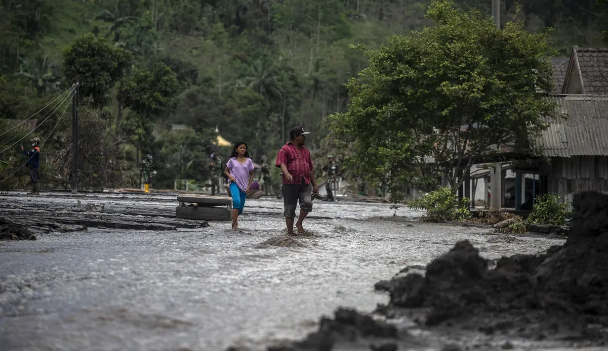 Warga melintasi air yang mengalir melewati rumah-rumah yang rusak di Dusun Kamar Kajang, Lumajang, Kamis (9/12/2021). Luapan air sungai bercampur material lahar dingin erupsi Gunung Semeru merendam puluhan rumah akibat diguyur hujan deras pada Selasa (7/12) dan Rabu (8/12) malam (Juni Kriswanto/AFP)