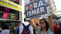 Seorang wanita membawa poster bertuliskan “Keluarkan Temer!” dalam unjuk rasa di Sao Paulo, Brasil, Rabu (2/8). Demonstrasi tersebut bertujuan untuk melengserkan Presiden Brasil Michel Temer yang diduga terkait kasus korupsi. (AP/Andre Penner)
