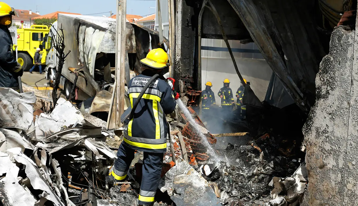 Petugas pemadam kebakaran memadamkan bara api dari pesawat kecil yang jatuh di dekat pasar swalayan daerah permukiman di Tires, Portugal, Senin (17/4). Empat orang yang berada di pesawat itu dan seorang lain di darat tewas seketika.( Bruno COLACO/AFP)