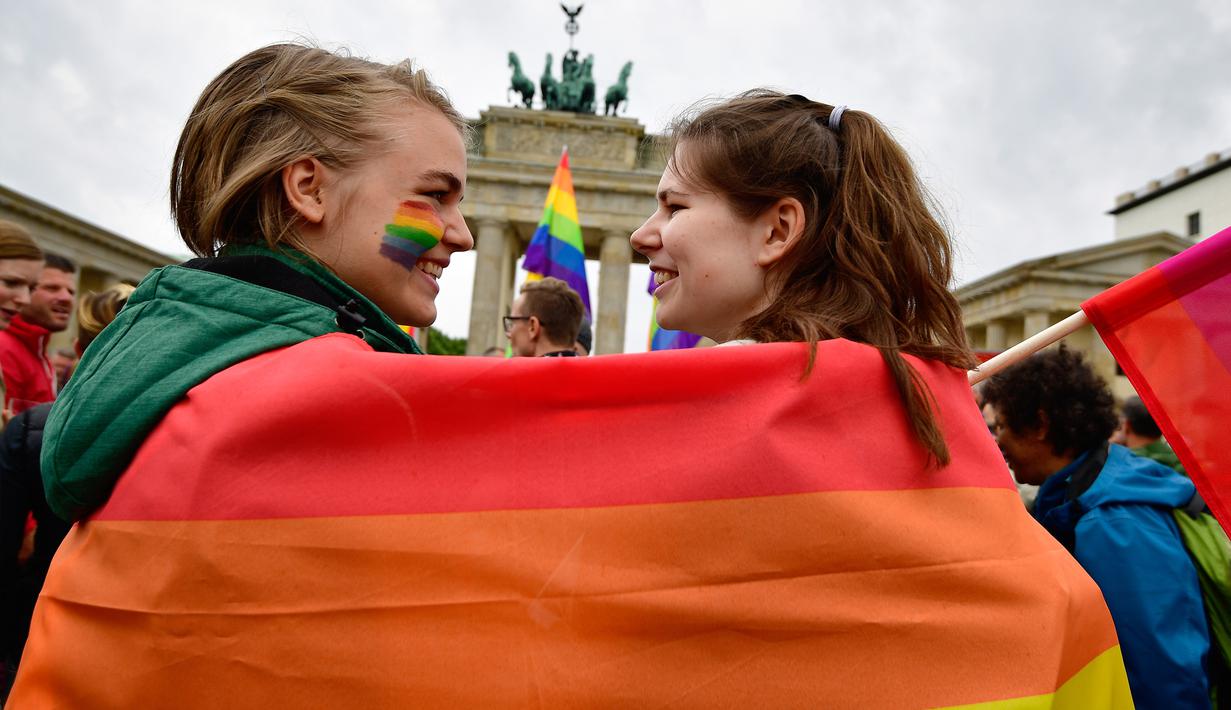 Dua wanita berselimut bendera pelangi saat demontrasi kaum LGBT di depan Gerbang Brandenburg di Berlin (30/6). Sebanyak 393 anggota parlemen Jerman menyetujui pernikahan sesama sejenis, dan 226 anggota lainnya menolaknya. (AFP Photo/Tobias Schwarz)