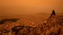 <p>Langit di Yunani selatan berubah menjadi oranye pada hari Selasa ketika awan debu yang tertiup melintasi Laut Mediterania dari Afrika Utara menyelimuti Acropolis dan landmark Athena lainnya. (Angelos TZORTZINIS / AFP)</p>