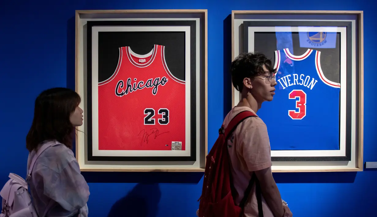 Pengunjung melihat jersey Michael Jordan (kiri) dan Allen Iverson (kanan) yang dipamerkan dalam pameran NBA (National Basketball Association) di Beijing, China, Senin (19/8/2019). (NICOLAS ASFOURI/AFP)