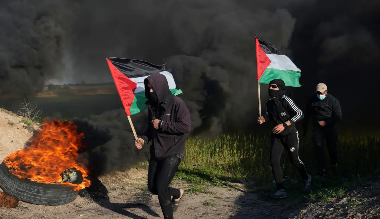 Demonstran berlari sambil mengibarkan bendera nasional mereka sementara yang lain membakar ban saat protes terhadap serangan militer Israel ke Kota Nablus, Tepi Barat, di sepanjang pagar perbatasan dengan Israel di sebelah timur Kota Gaza, 22 Februari 2023. Para pejabat Palestina mengatakan sejumlah warga Palestina telah terbunuh dan lebih dari seratus orang terluka dalam serangan tentara Israel yang jarang terjadi di Tepi Barat. (AP Photo/Adel Hana)