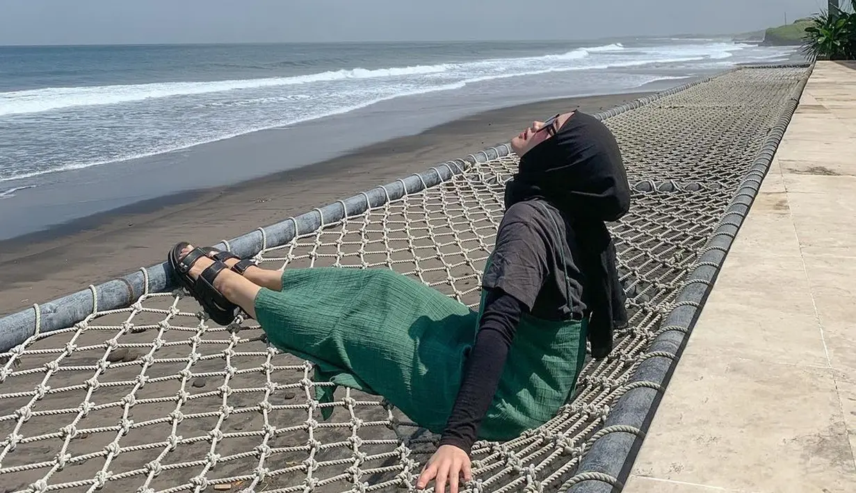 Mengenakan terusan hijau tua yang dikombinasikan dengan luaran hitam dan hijab berwarna senada, Putri Delina duduk di bibir laut beralaskan hammock. Ia menatap cakrawala yang memayungi laut. Bersama foto ini, ia mencuit soal kebahagiaan dan syukur, “Bukan kebahagiaan yang membuat kita bersyukur. Syukurlah yang membawa kita kepada kebahagiaan.” (Foto: Dok. Instagram @putridelinaa)