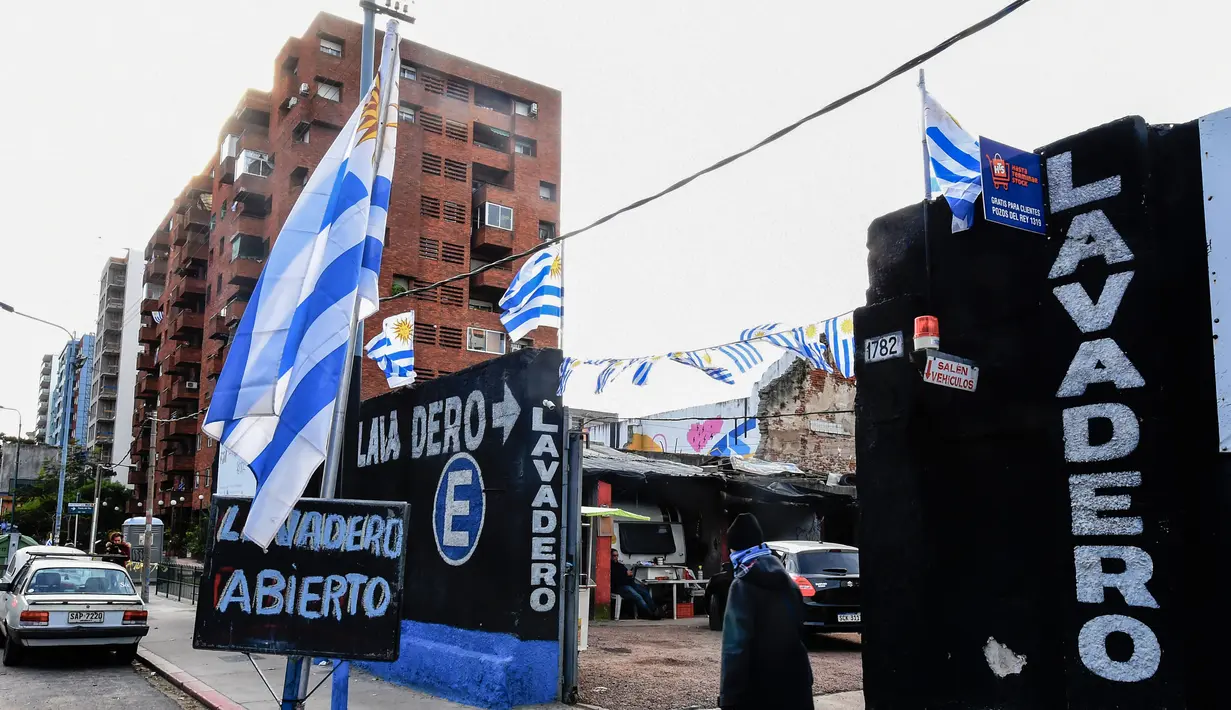 Pejalan kaki milintas di depan tempat cuci mobil yang dihiasi bendera Uruguay di Montevideo (4/7). Uruguay dan Prancis akan bertanding pada babak 8 besar Piala Dunia 2018 di Nizhny Novgorod Stadium, Rusia. AFP Photo/Miguel Rojo)