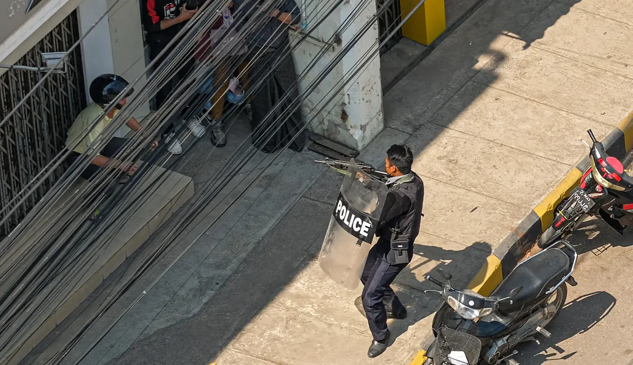 Seorang polisi mengarahkan senjatanya ke orang-orang di Taunggyi, sebuah kota di Negara Bagian Shan (28/2/2021).  Myanmar berada dalam kekacauan sejak tentara merebut kekuasaan dan menahan pemimpin pemerintah terpilih Aung San Suu Kyi. (AFP/STR)
