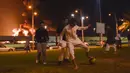 Anak-anak muda bermain sepak bola saat asap dan api membubung dari fasilitas minyak Aramco pada kejauhan menyusul laporan serangan pemberontak Yaman di Kota Jeddah, Arab Saudi, 25 Maret 2022. Pemberontak Yaman mengatakan mereka menyerang fasilitas minyak Arab Saudi tersebut. (AFP)