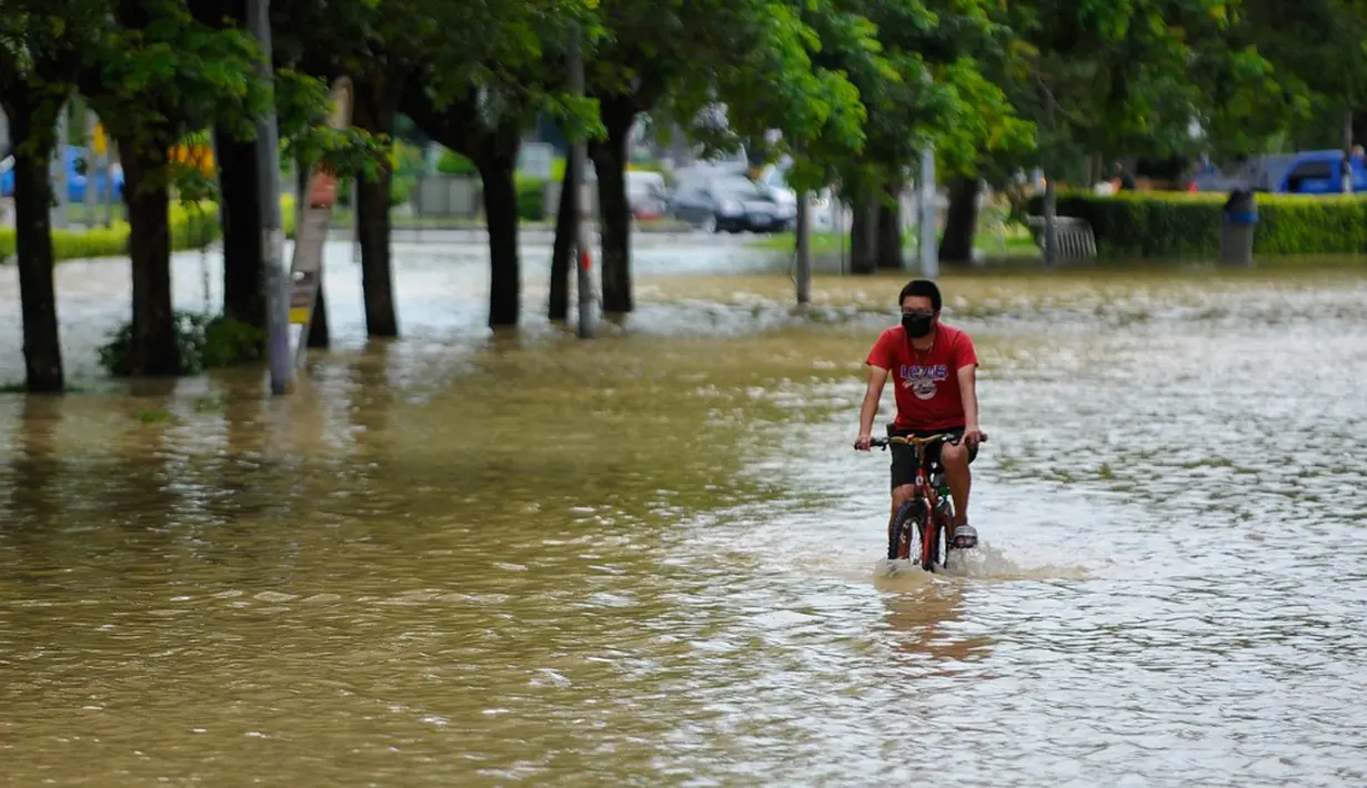 Seorang pria bersepeda menerjang banjir di Batu Berendam, Malaka, Malaysia, 3 Januari 2022. Tercatat ada tujuh negara bagian Malaysia yang diterjang banjir pada 2 Januari 2022. (NAZRULHAD HASHIM/AFP)