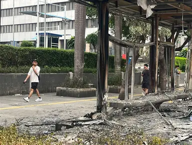 Warga melintas di sisi salah satu halte yang hangus di Jalan Jenderal Sudirman, Jakarta, Sabtu (30/8/2025). (merdeka.com/Arie Basuki)