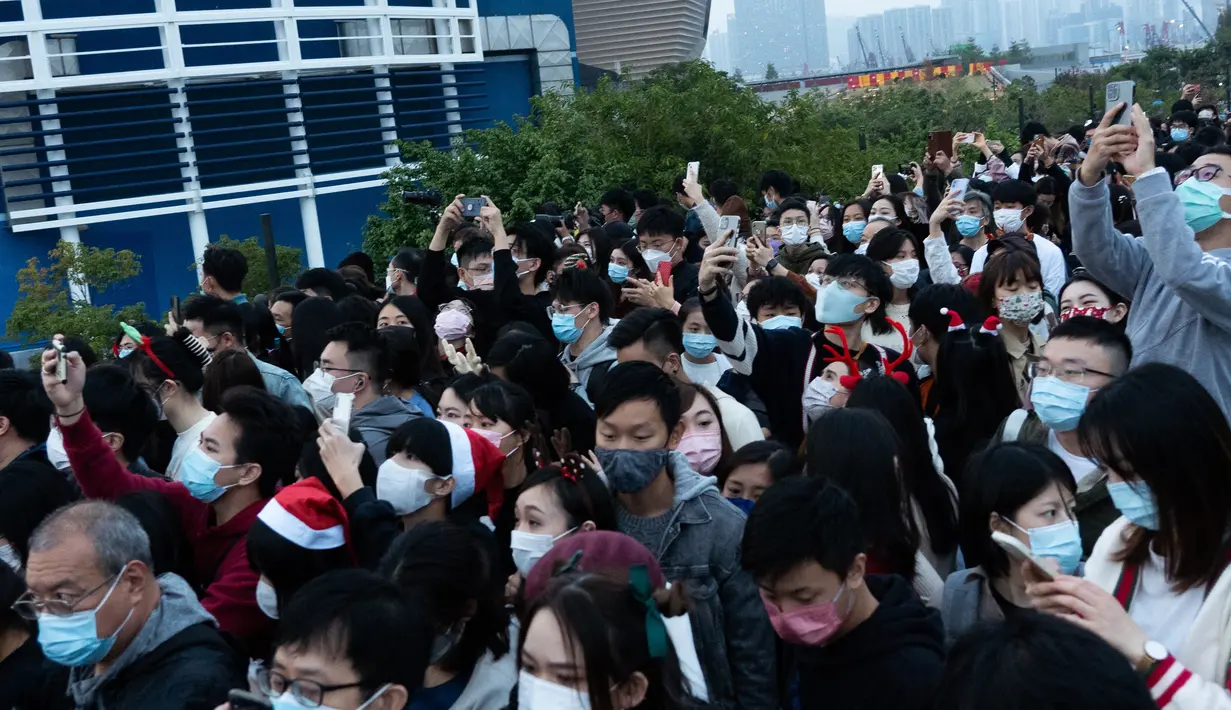 Orang-orang mengambil foto pohon Natal raksasa selama Natal di distrik budaya West Kowloon di Hong Kong (25/12/2021). Pohon Natal raksasa didekorasi secara glamor dengan karangan bunga dan ornamen, berkilauan dengan lampu meriah yang cerah. (AFP/Bertha Wang)