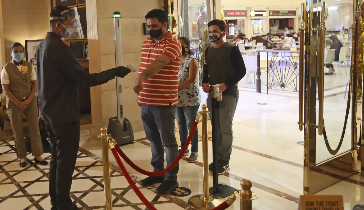 Seorang karyawan memeriksa suhu pejuang COVID-19 dan keluarganya yang tiba saat bioskop dibuka kembali dengan pemutaran khusus untuk mereka di bioskop PVR di New Delhi, India (15/101/2020). Bioskop telah menerapkan protokol kesehatan yang ketat. (AP Photo/Manish Swarup)