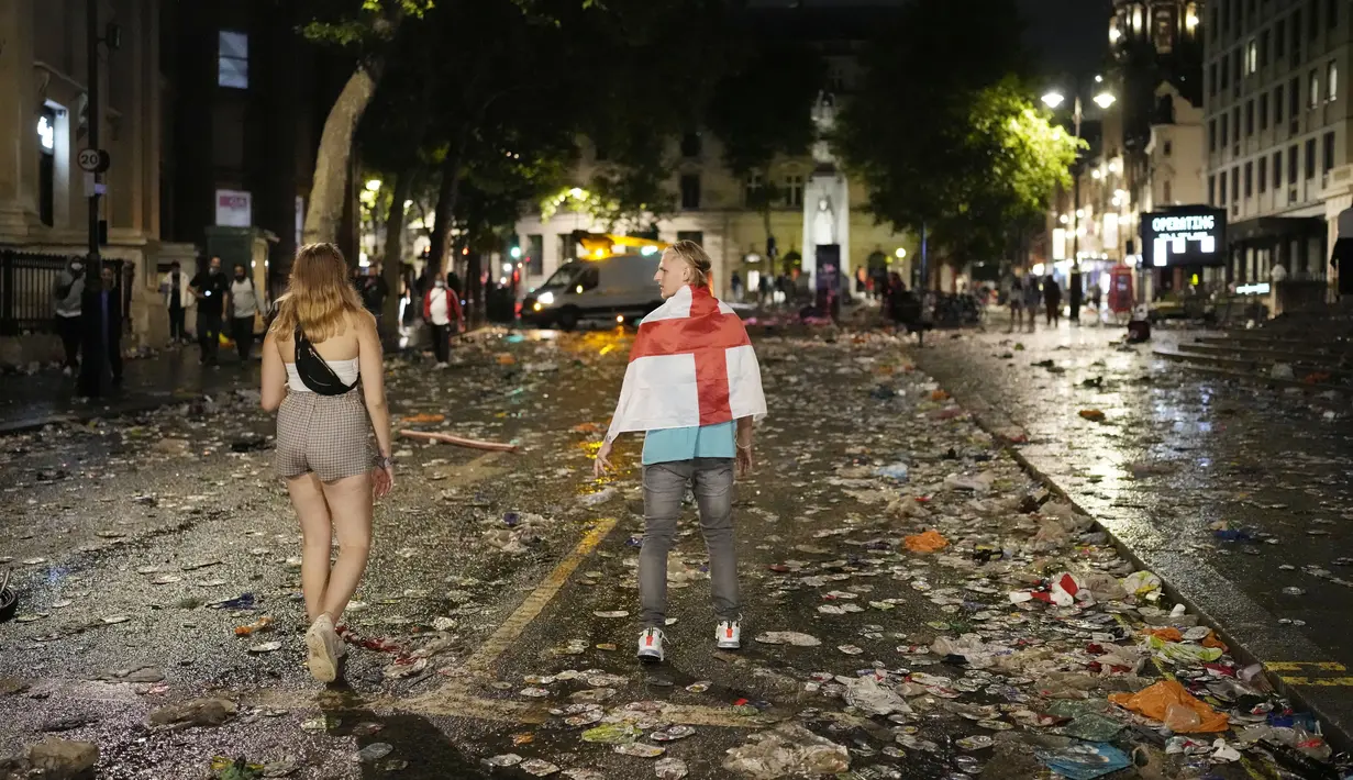 Dua fans Timnas Inggris berjalan diantara sampah yang berserakan di Kota London paska final Euro 2020 antara Timnas Inggris melawan Italia. (Foto:AP/Matt Dunham)