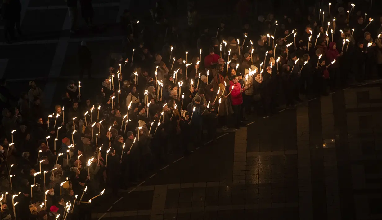 Orang-orang memegang obor saat demonstrasi untuk Ukraina yang diselenggarakan oleh Greenpeace di Heroes Square, Budapest, Hungaria, 9 Maret 2022. Invasi Rusia ke Ukraina telah memicu migrasi massal terbesar di Eropa dalam beberapa dekade. (AP Photo/Anna Szilagyi)