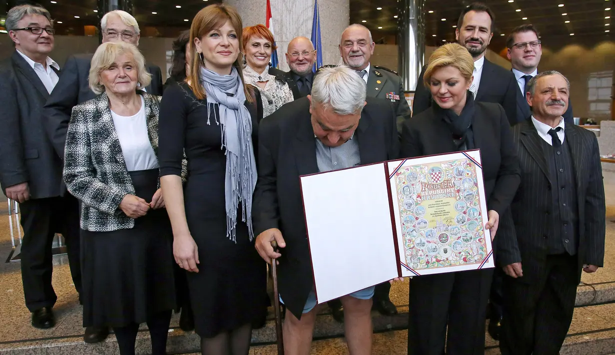 Kepala Komisi HAM Helsinki Kroasia, Ivan Zvonimir Cicak harus menahan malu ketika celananya melorot tepat saat sesi foto dengan Presiden Kroasia Kolinda Grabar-Kitrarovic di Zagreb, Selasa (8/12). (STRINGER / AFP)